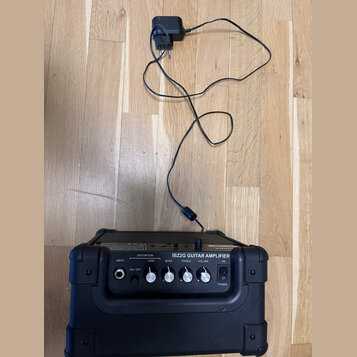 Černý kytarový zesilovač s nápisem IBZ2G GUITAR AMPLIFIER. Na ovládacím panelu jsou vstupy a knofíky s popisky INPUT, DISTORTION (ON / OFF), GAIN, BA…