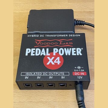 Černý napájecí adaptér s nápisy HYBRID DC TRANSFORMER DESIGN, Voodoo Lab a PEDAL POWER X4. Spodní část obsahuje čtyři výstupy označené jako ISOLATED…