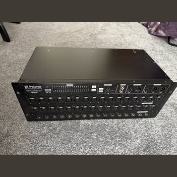 Černý rackový stagebox značky PreSonus s nápisem STUDIOLIVE RM32. Zařízení obsahuje řadu kombinovaných konektorů pro vstupy označených čísly 1 až 32…