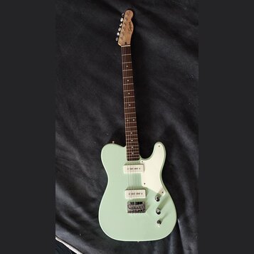 Světle zelená elektrická kytara s bílým pickguardem a hnědým hmatníkem. Na hlavě je viditelné logo Squier. Kytara má dva snímače a tři ovládací knofl…