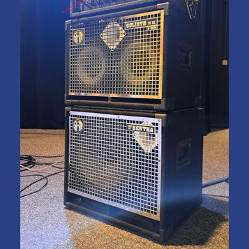 Dvě černé basové reproduktorové skříně naskládané na sebe. Horní skříň má stříbrnou mřížku s nápisy GOLIATH III a 8 OHM a logem značky Warwick. Spodn…