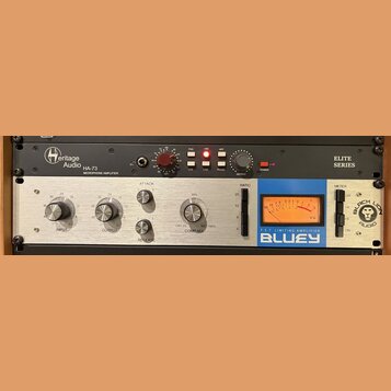 Fotografie zachycuje dvě rackové jednotky. Horní černý přístroj má nápisy Heritage Audio, HA-73 MICROPHONE AMPLIFIER a ELITE SERIES. Dolní stříbrný p…