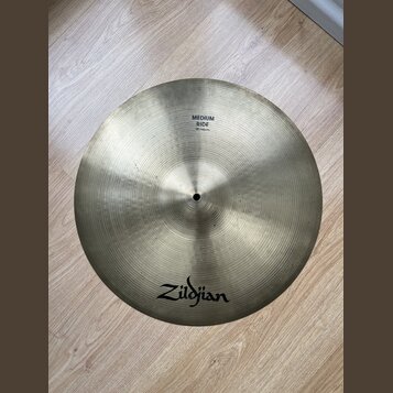 Kruhový činely v zlatavé barvě s viditelným koncentrickým broušením povrchu. Na činely jsou černé nápisy Zildjian a MEDIUM RIDE 18"/46cm. Povrch vyka…