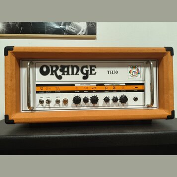 Kytarový zesilovač v oranžovém vinylu s bílým předním panelem. Na panelu je velký nápis ORANGE a označení modelu TH30 spolu s logem. Zesilovač obsahu…