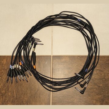Sada černých audio kabelů s 6,3mm jack konektory. Některé konektory mají barevné značky v modré, oranžové a bílé barvě. Kabely jsou svinuté do kruhu…