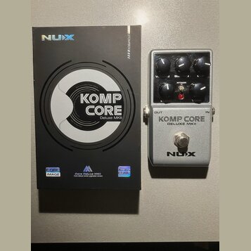 Na fotografii je stříbrný efektový pedál s černými ovládacími knoflíky a přepínačem. Na pedálu jsou nápisy KOMP CORE DELUXE MKII a logo NUX. Vedle pe…