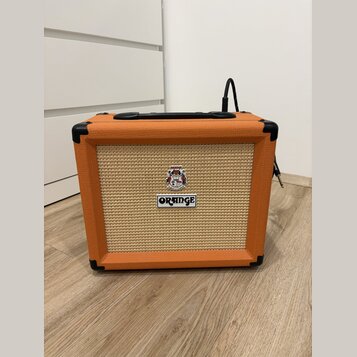 Kytarový kombo zesilovač s oranžovým texturovaným povrchem a béžovou přední síťovkou. Na mřížce je umístěno logo ORANGE a nad ním kulatý štítek s neč…