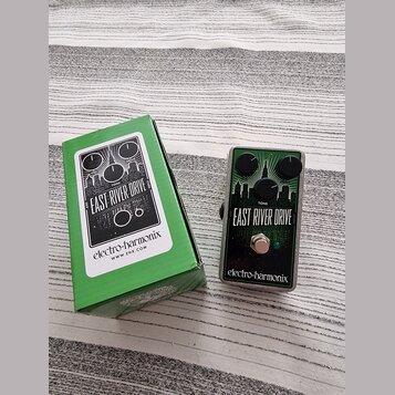 Kytarový efekt v kovovém šasi s nápisem EAST RIVER DRIVE a logem electro-harmonix. Pedál má tři černé ovládací knoflíky, zelený spínací tlačítko a gr…