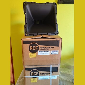 Černý plastový akustický horn umístěný na dvou hnědých kartonových krabicích. Na krabicích je vidět logo RCF a nápisy PRECISION TRANSDUCERS, HF950 HO…