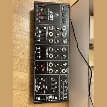Černý elektronický syntetizátor s nápisem "behringer CAT" a přívstkem "electronic music synthesizer". Přední panel obsahuje množství bílých posuvníků…